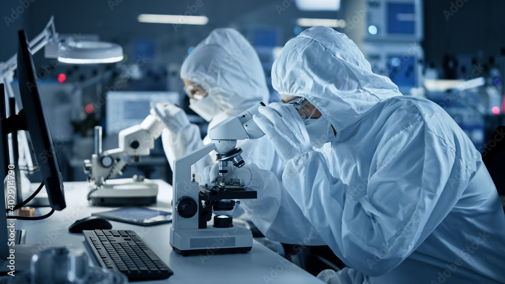 Research Factory Cleanroom: Engineers / Scientists wearing Coveralls and Gloves Use Microscopes to Inspect Motherboard Microprocessor Components, Developing High Tech Modern Electronics Research Factory Cleanroom: Engineers / Scientists wearing Coveralls and Gloves Use Microscopes to Inspect Motherboard Microprocessor Components, Developing High Tech Modern Electronics