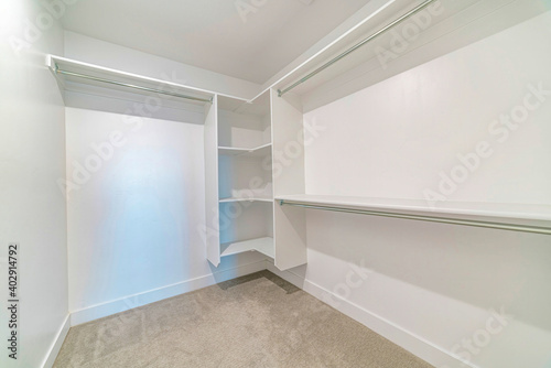 Interior of a walk in closet with shelves and clothes rod mounted on white wall