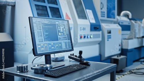 Factory Cleanroom: On the Desk Personal Computer Showing Infrastructure System Control on its Display. In Background CNC Machinery, Professionals Use Robot Arm on Production Line.