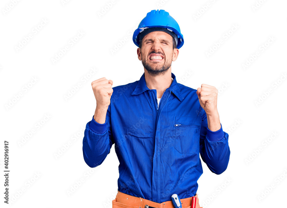 Young handsome man wearing worker uniform and hardhat excited for success with arms raised and eyes closed celebrating victory smiling. winner concept.