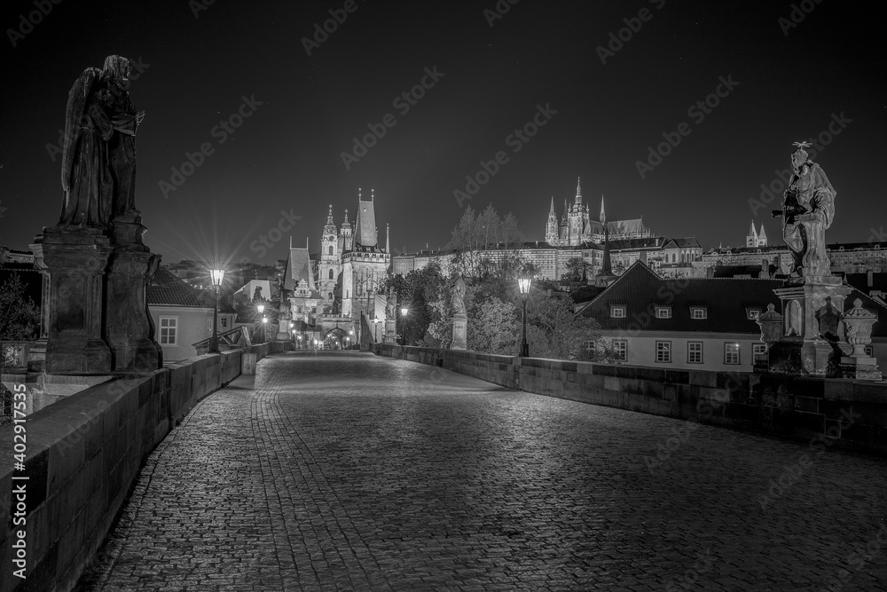 Obraz premium Empty Charles Bridge in the center of Prague during first wave of Covid-19 pandemy in the night with blue sky and yellow lights, Czechia, Europe