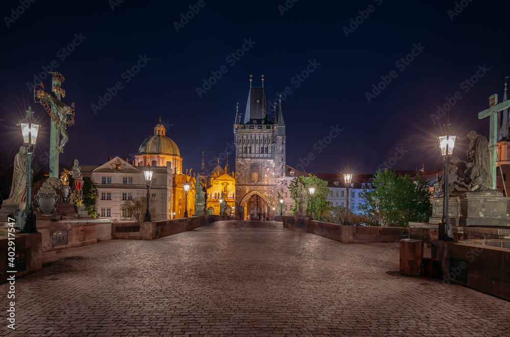 Empty Charles Bridge in the center of Prague during first wave of Covid-19 pandemy in the night with blue sky and yellow lights, Czechia, Europe