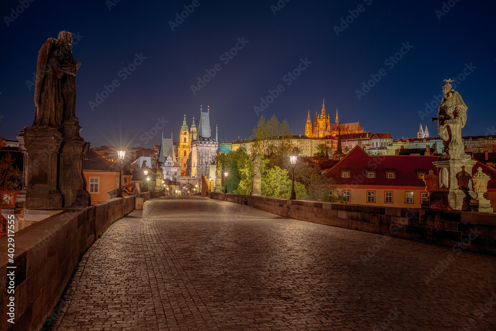 Empty Charles Bridge in the center of Prague during first wave of Covid-19 pandemy in the night with blue sky and yellow lights, Czechia, Europe