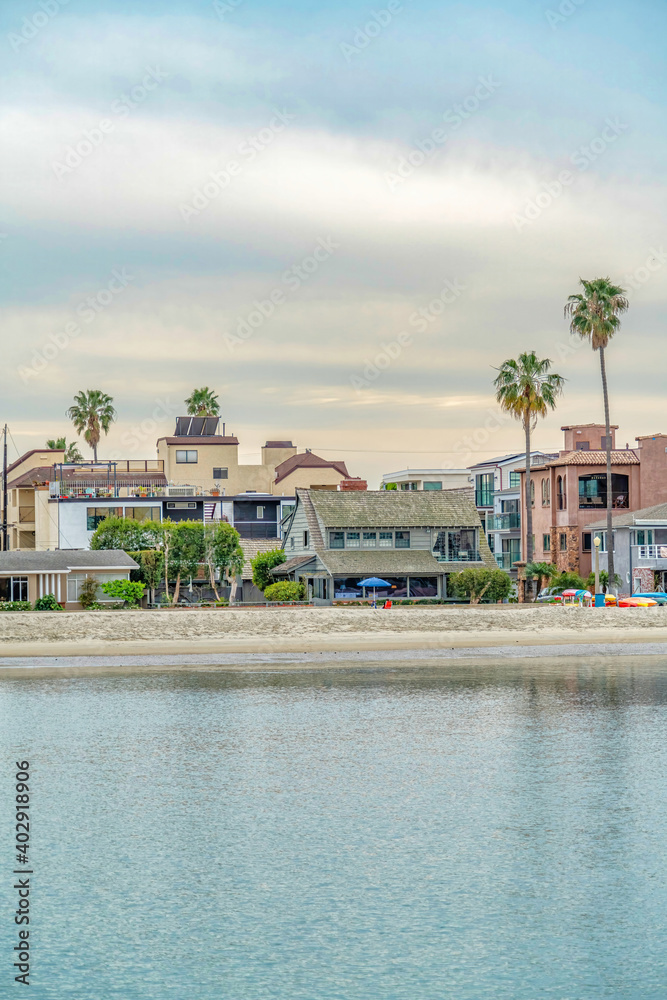 Beach with beautiful waterfront houses and palm trees against cloudy skyscape