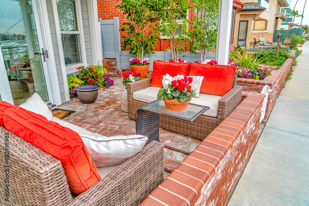 Wicker bench and glass table at patio of home with colorful pillows and flowers