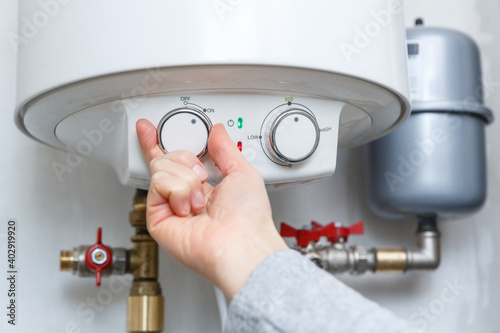 Female hand turning on electric water heater (boiler).