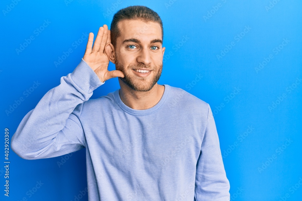 Young caucasian man wearing casual clothes smiling with hand over ear listening and hearing to rumor or gossip. deafness concept. Young caucasian man wearing casual clothes smiling with hand over ear listening and hearing to rumor or gossip. deafness concept.