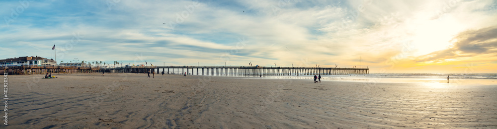 Panoramic view of  Pismo Beach at sunset. Wide sandy beach, a long wooden pier, ocean view and beautiful cloudy sky on background