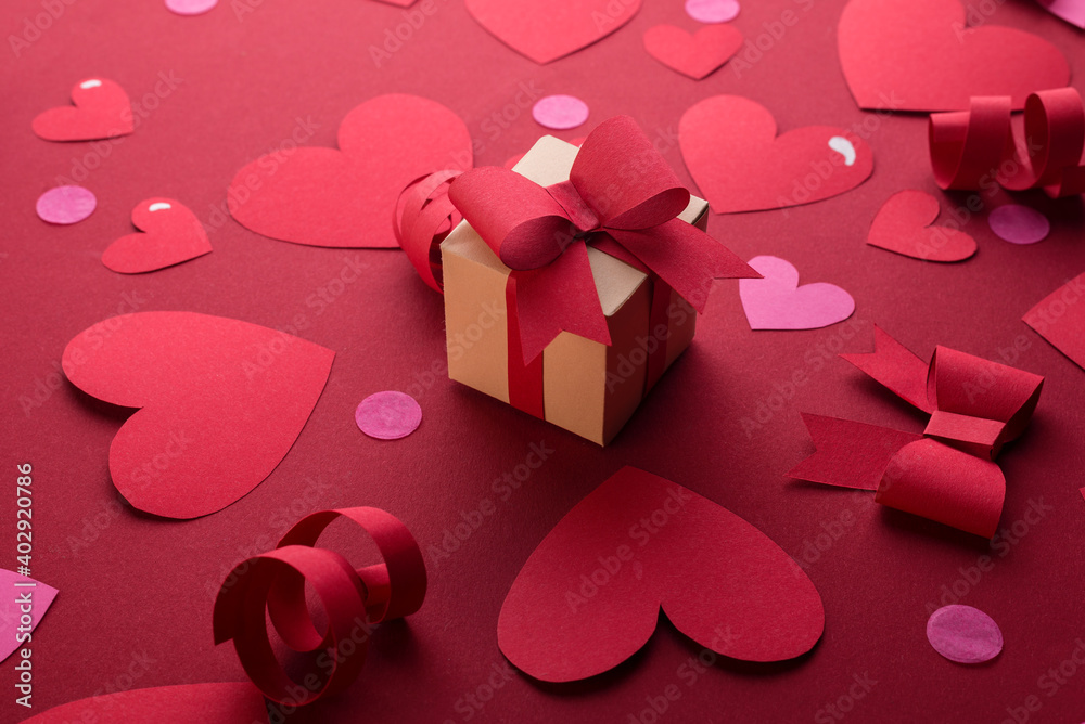 Happy st. Valentines day concept with craft paper gift box, red paper hearts, bows against dark red background with empty space for text. Happy st. Valentines day concept with craft paper gift box, red paper hearts, bows against dark red background with empty space for text.