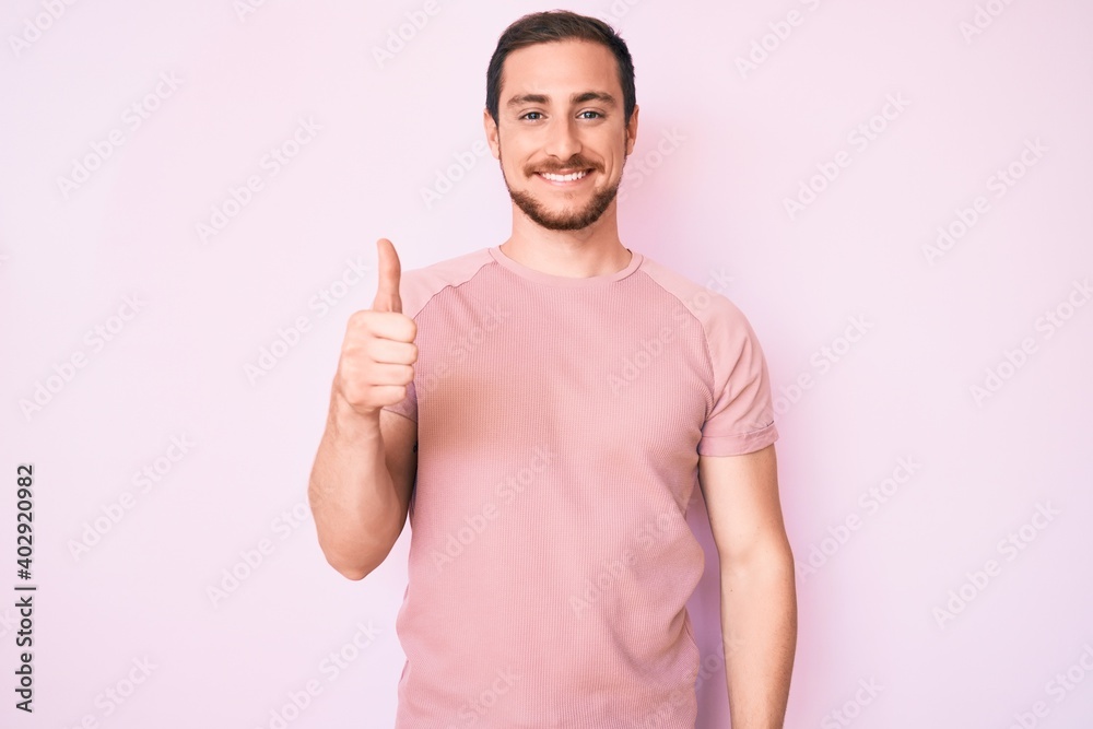 Young handsome man wearing casual tshirt smiling happy and positive, thumb up doing excellent and approval sign Young handsome man wearing casual tshirt smiling happy and positive, thumb up doing excellent and approval sign