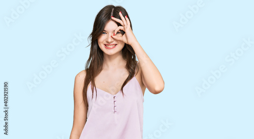 Young beautiful caucasian girl wearing casual clothes doing ok gesture with hand smiling, eye looking through fingers with happy face.