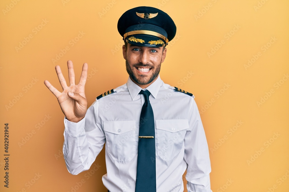 Handsome hispanic man wearing airplane pilot uniform showing and pointing up with fingers number four while smiling confident and happy. - obrazy, fototapety, plakaty 