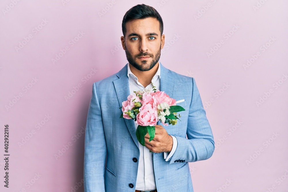 Young hispanic businessman wearing business jacket holding flowers thinking attitude and sober expression looking self confident Young hispanic businessman wearing business jacket holding flowers thinking attitude and sober expression looking self confident