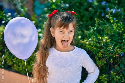 Adorable caucasian child girl with tongue out playing with ballon at the park.