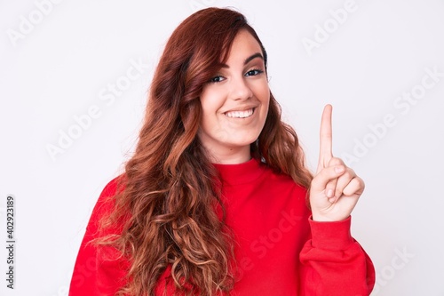 Young beautiful woman wearing casual clothes showing and pointing up with finger number one while smiling confident and happy.
