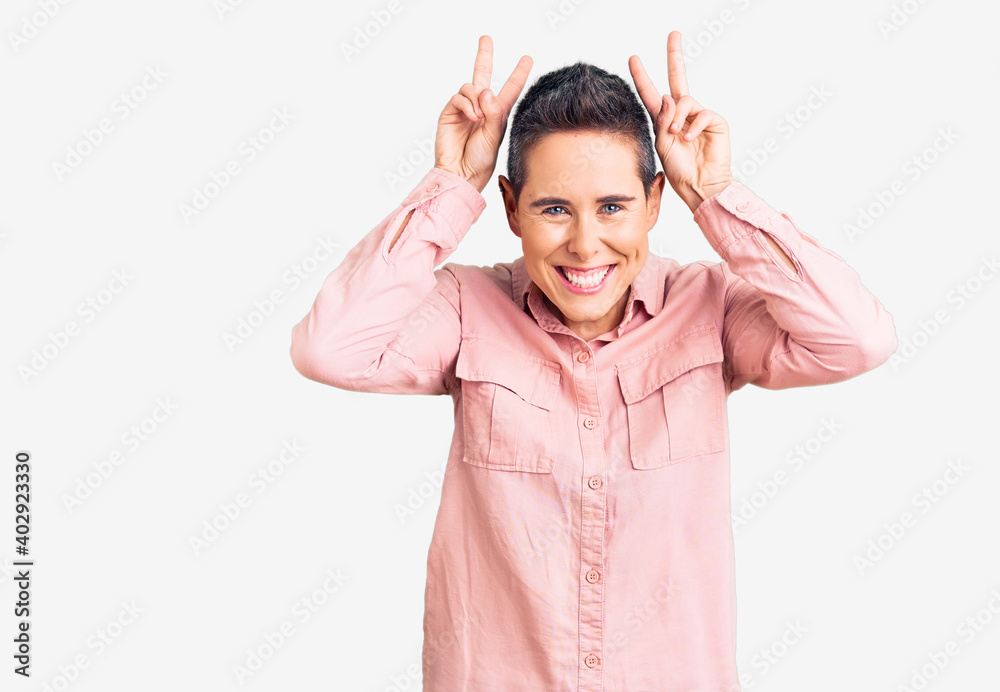 Young woman with short hair wearing casual clothes posing funny and crazy with fingers on head as bunny ears, smiling cheerful Young woman with short hair wearing casual clothes posing funny and crazy with fingers on head as bunny ears, smiling cheerful