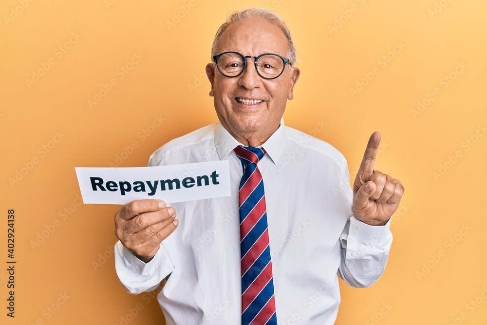 Senior caucasian man holding repayment word paper smiling with an idea or question pointing finger with happy face, number one Senior caucasian man holding repayment word paper smiling with an idea or question pointing finger with happy face, number one
