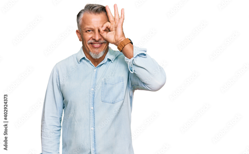 Middle age grey-haired man wearing casual clothes doing ok gesture with hand smiling, eye looking through fingers with happy face. Middle age grey-haired man wearing casual clothes doing ok gesture with hand smiling, eye looking through fingers with happy face.