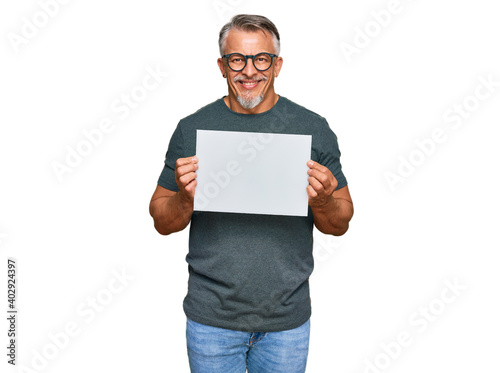 Middle age grey-haired man holding blank empty banner looking positive and happy standing and smiling with a confident smile showing teeth
