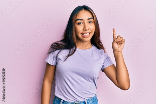 Young latin woman wearing casual clothes smiling with an idea or question pointing finger up with happy face, number one