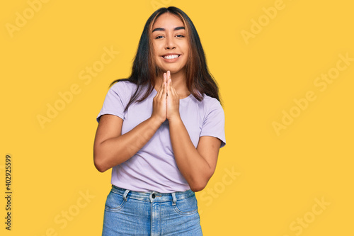 Young latin woman wearing casual clothes praying with hands together asking for forgiveness smiling confident.