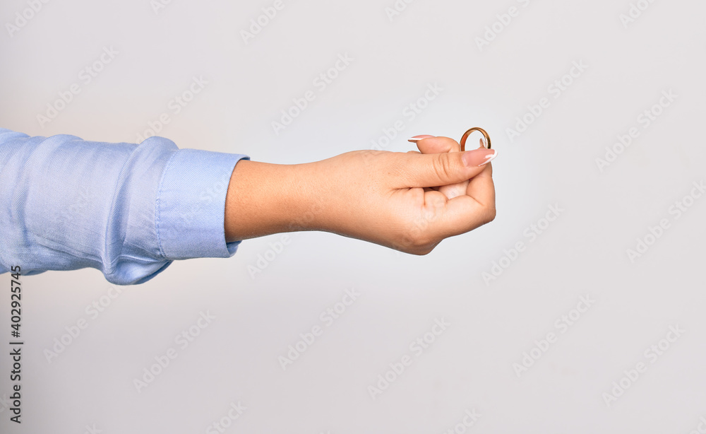 Hand of caucasian young woman holding golden marriage ring over isolated white background
