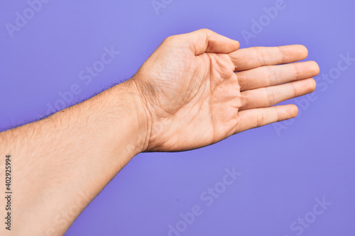 Hand of caucasian young man showing fingers over isolated purple background stretching and reaching with open hand for handshake, showing palm