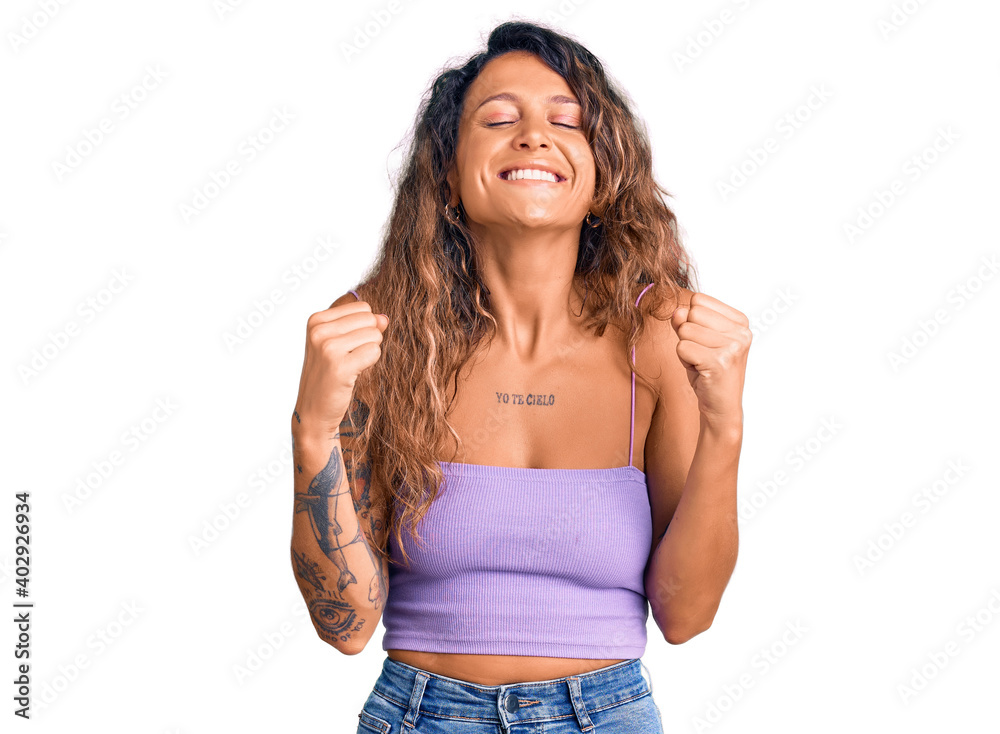 Young hispanic woman with tattoo wearing casual clothes excited for success with arms raised and eyes closed celebrating victory smiling. winner concept. Young hispanic woman with tattoo wearing casual clothes excited for success with arms raised and eyes closed celebrating victory smiling. winner concept.