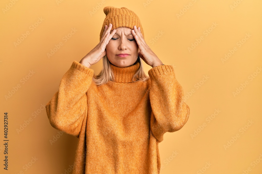 Middle age caucasian woman wearing wool winter sweater and hat suffering from headache desperate and stressed because pain and migraine. hands on head. Middle age caucasian woman wearing wool winter sweater and hat suffering from headache desperate and stressed because pain and migraine. hands on head.