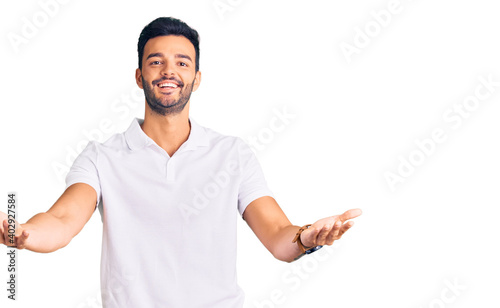 Young handsome hispanic man wearing casual clothes smiling cheerful offering hands giving assistance and acceptance.