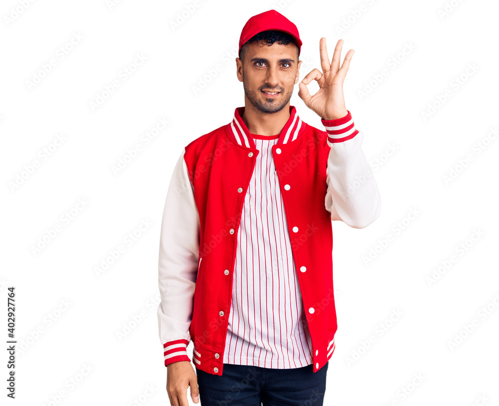 Young hispanic man wearing baseball uniform smiling positive doing ok sign with hand and fingers. successful expression. Young hispanic man wearing baseball uniform smiling positive doing ok sign with hand and fingers. successful expression.