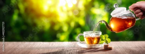 Panel kuchenny z motywem black tea with mint flavor pouring from glass teapot into double sided wall cup on wooden table with green natural blurred background