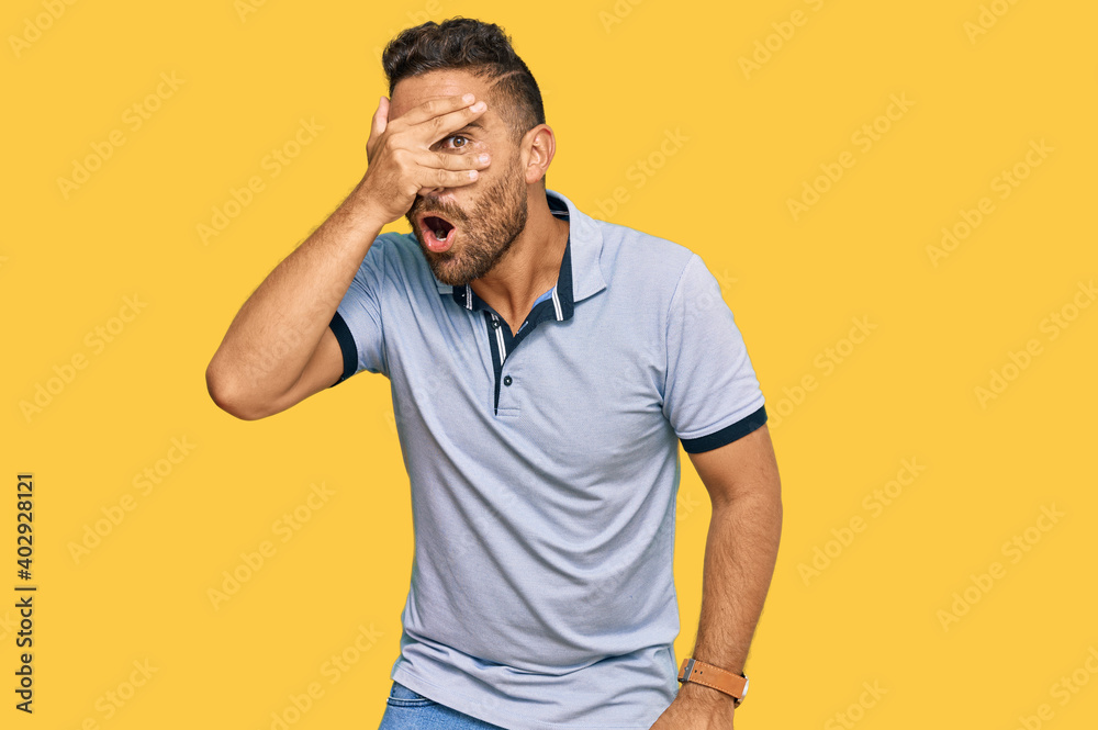 Handsome man with beard wearing casual clothes peeking in shock covering face and eyes with hand, looking through fingers with embarrassed expression. Handsome man with beard wearing casual clothes peeking in shock covering face and eyes with hand, looking through fingers with embarrassed expression.