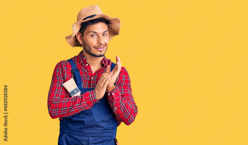 Handsome latin american young man weaing handyman uniform clapping and applauding happy and joyful, smiling proud hands together