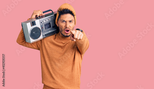 Handsome latin american young man holding boombox, listening to music pointing displeased and frustrated to the camera, angry and furious with you