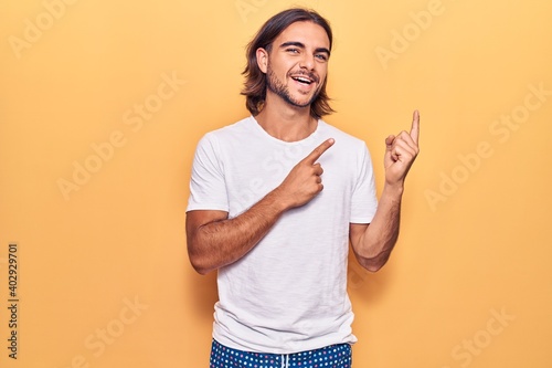 Young handsome man wearing casual clothes smiling and looking at the camera pointing with two hands and fingers to the side.