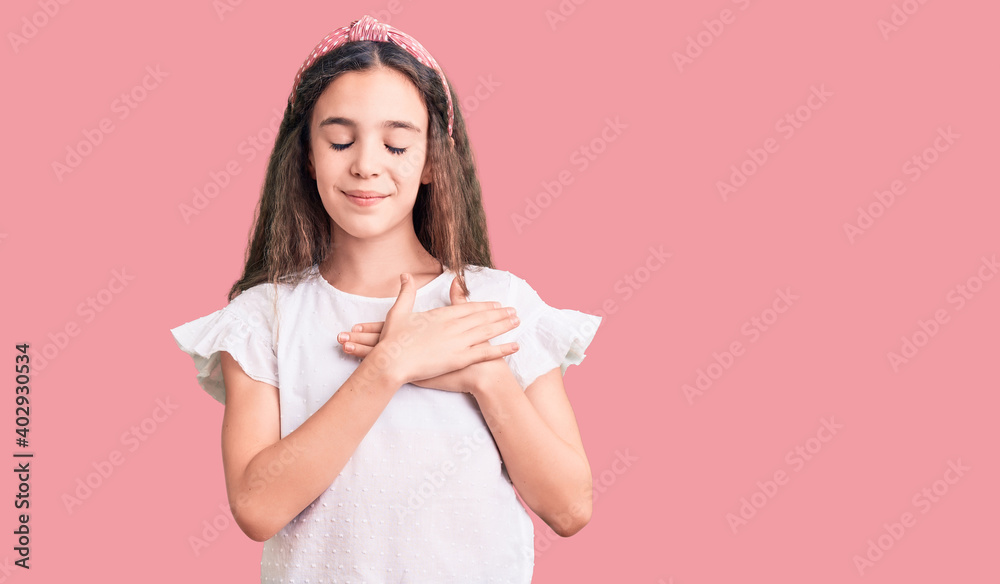 Cute hispanic child girl wearing casual white tshirt smiling with hands on chest with closed eyes and grateful gesture on face. health concept. Cute hispanic child girl wearing casual white tshirt smiling with hands on chest with closed eyes and grateful gesture on face. health concept.