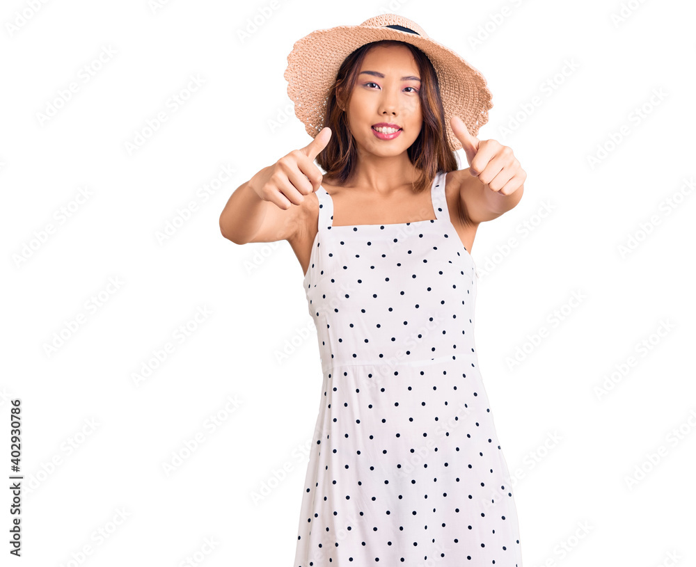 Young beautiful chinese girl wearing summer hat approving doing positive gesture with hand, thumbs up smiling and happy for success. winner gesture. Young beautiful chinese girl wearing summer hat approving doing positive gesture with hand, thumbs up smiling and happy for success. winner gesture.