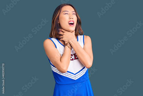 Foto Young beautiful chinese girl wearing cheerleader uniform shouting suffocate because painful strangle