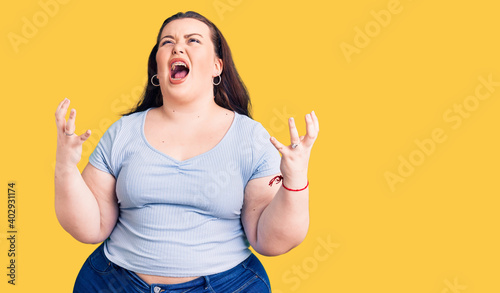 Young plus size woman wearing casual clothes crazy and mad shouting and yelling with aggressive expression and arms raised. frustration concept.