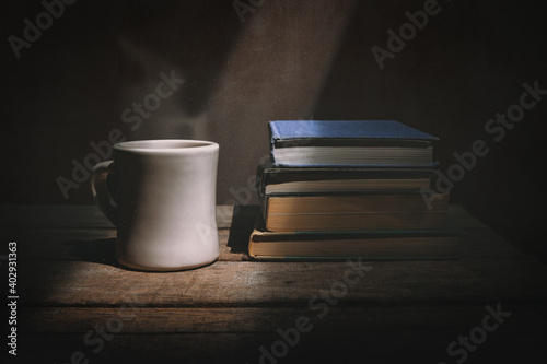 Steaming cup of coffee with a stack of books illuminated by a shaft of light