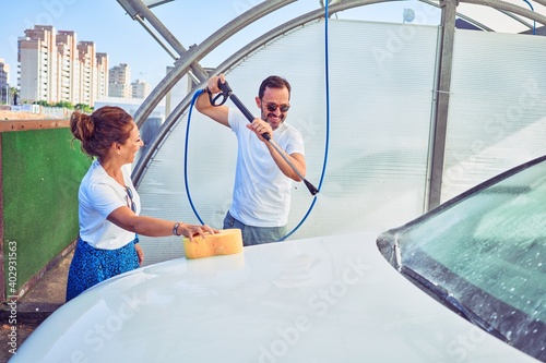 Middle age beautiful couple wearing casual clothes and smiling happy. Standing with smile on face washing car using water pistol and sponge. © Krakenimages.com