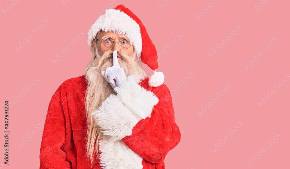 Old senior man with grey hair and long beard wearing traditional santa claus costume asking to be quiet with finger on lips. silence and secret concept. Old senior man with grey hair and long beard wearing traditional santa claus costume asking to be quiet with finger on lips. silence and secret concept.