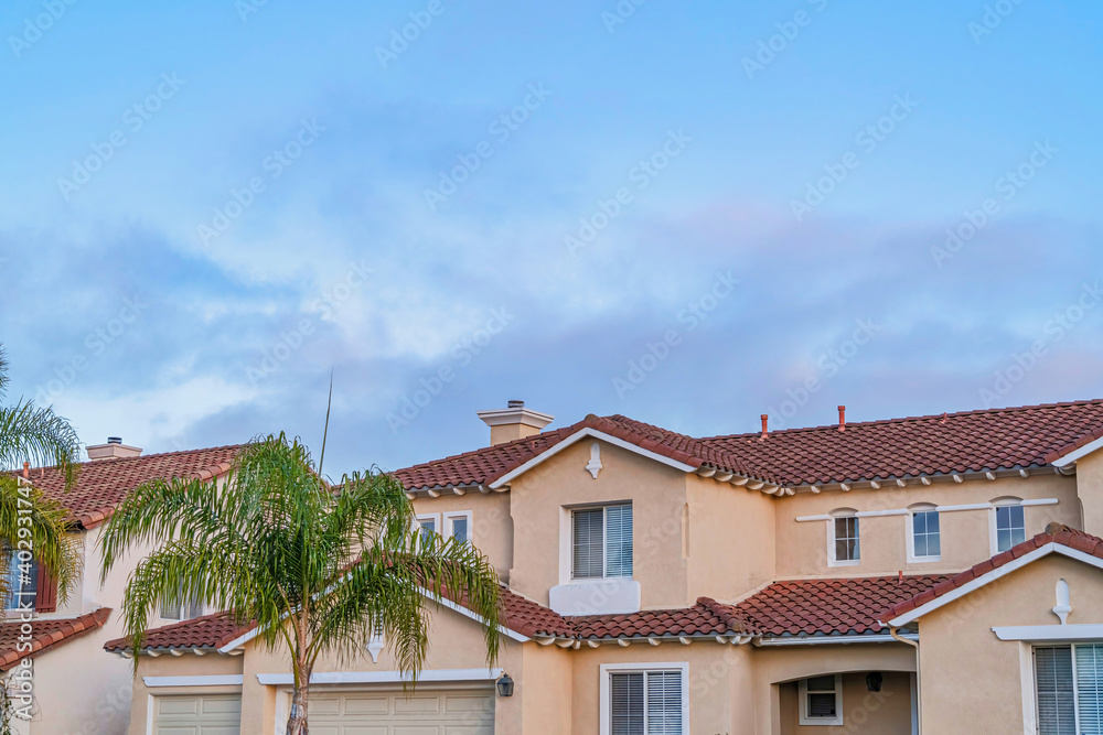 Houses with red tile roofs and beige wall against cloudy sky in San Diego CA