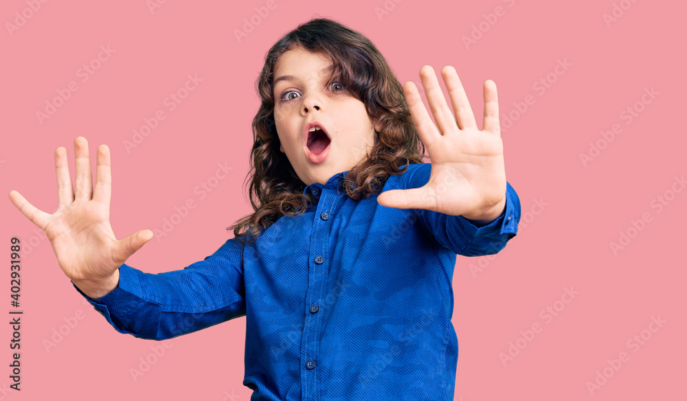 Cute child with long hair wearing casual clothes afraid and terrified with fear expression stop gesture with hands, shouting in shock. panic concept.