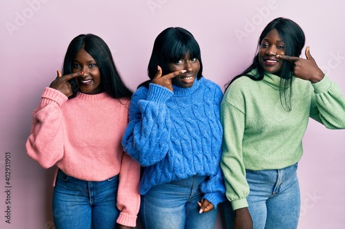 Three young african american friends wearing wool winter sweater pointing with hand finger to face and nose, smiling cheerful. beauty concept