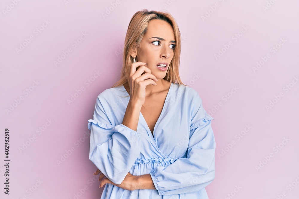 Beautiful blonde woman wearing summer dress thinking concentrated about doubt with finger on chin and looking up wondering Beautiful blonde woman wearing summer dress thinking concentrated about doubt with finger on chin and looking up wondering