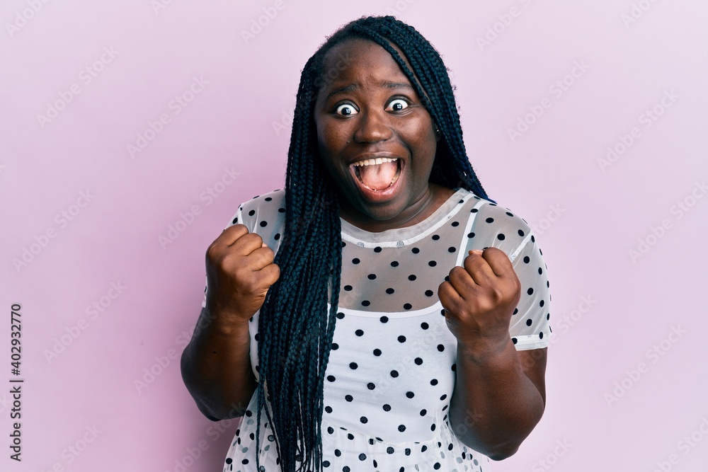 Young black woman with braids wearing casual clothes celebrating surprised and amazed for success with arms raised and open eyes. winner concept. Young black woman with braids wearing casual clothes celebrating surprised and amazed for success with arms raised and open eyes. winner concept.