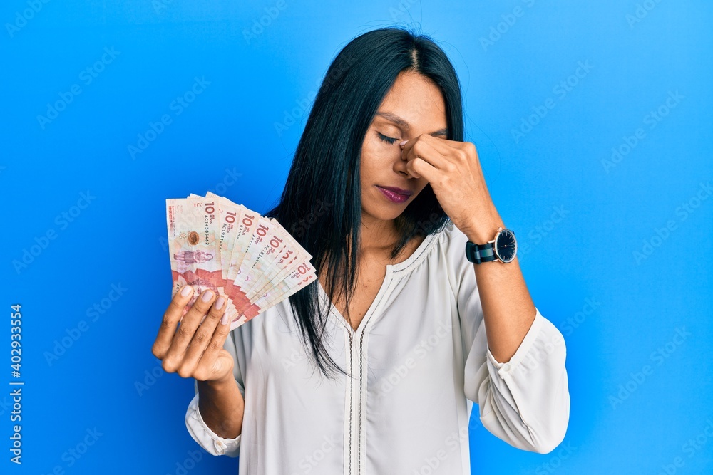 Young african american woman holding 10 colombian pesos banknotes tired rubbing nose and eyes feeling fatigue and headache. stress and frustration concept. Young african american woman holding 10 colombian pesos banknotes tired rubbing nose and eyes feeling fatigue and headache. stress and frustration concept.