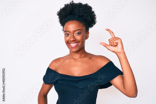 Young african american woman wearing casual clothes smiling and confident gesturing with hand doing small size sign with fingers looking and the camera. measure concept.